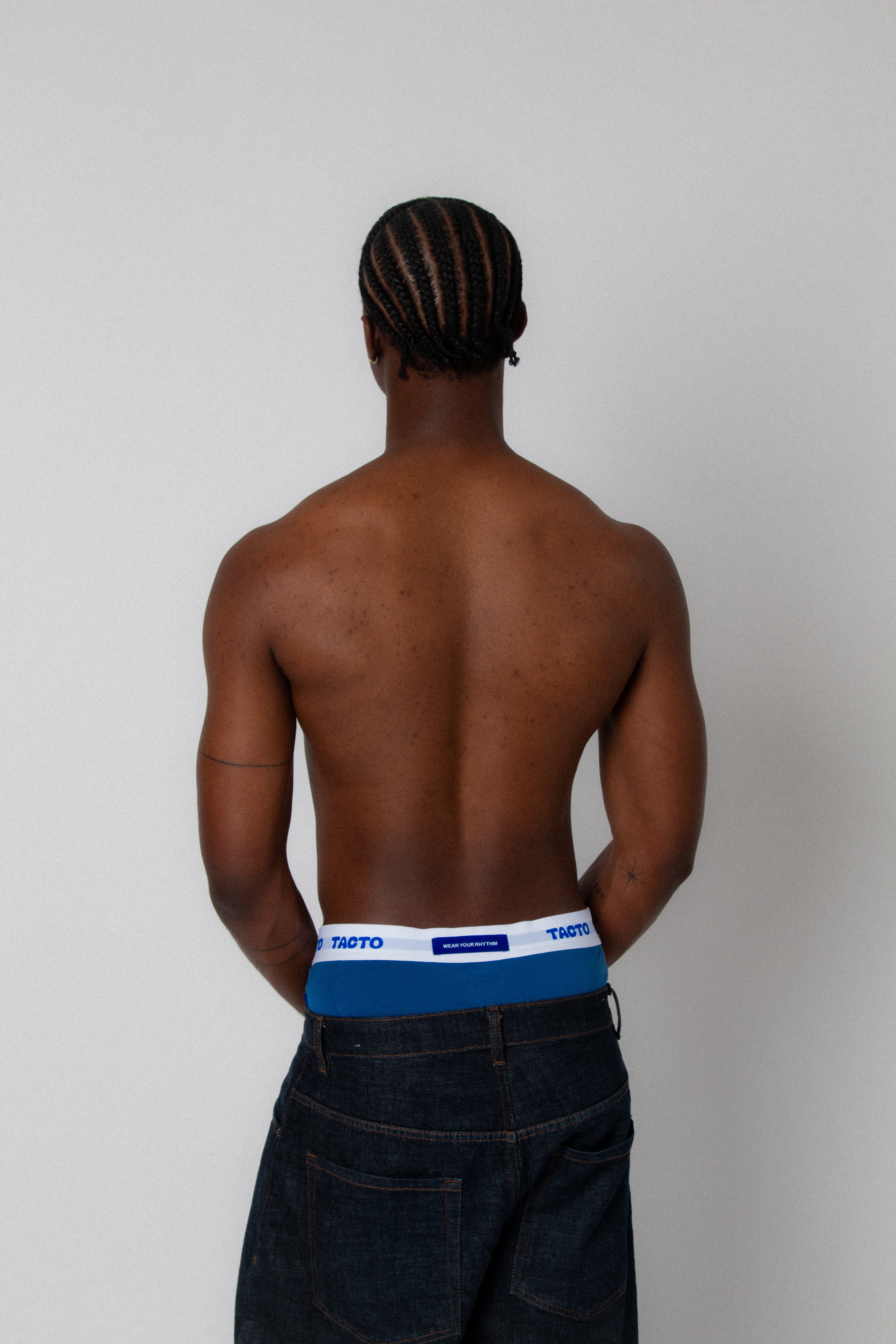 Man wearing a blue underwear with a visible brand logo on a plain background. TACTO Collective underwear.
