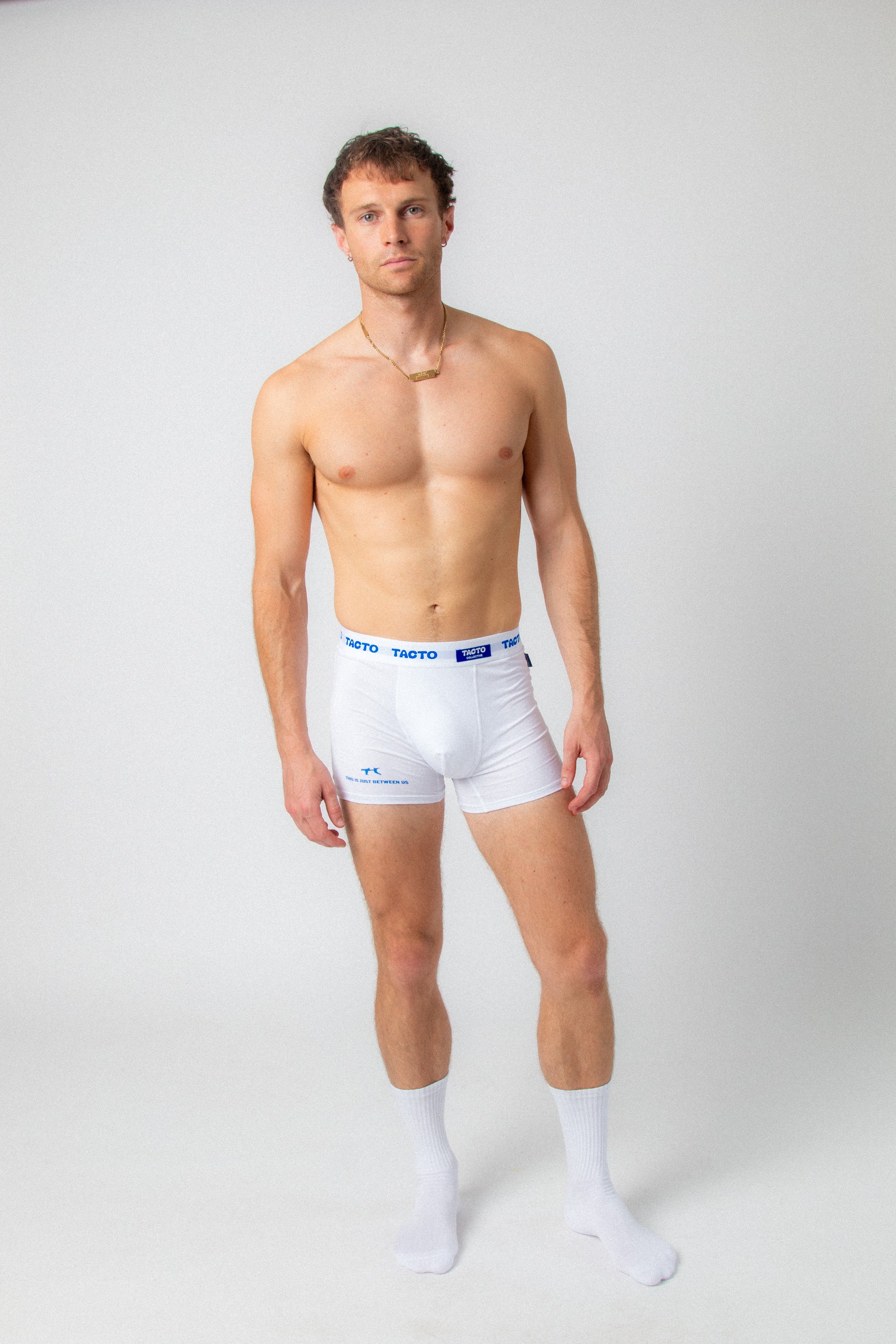 Man wearing white boxer briefs with a visible brand logo on a plain background. Tacto underwear