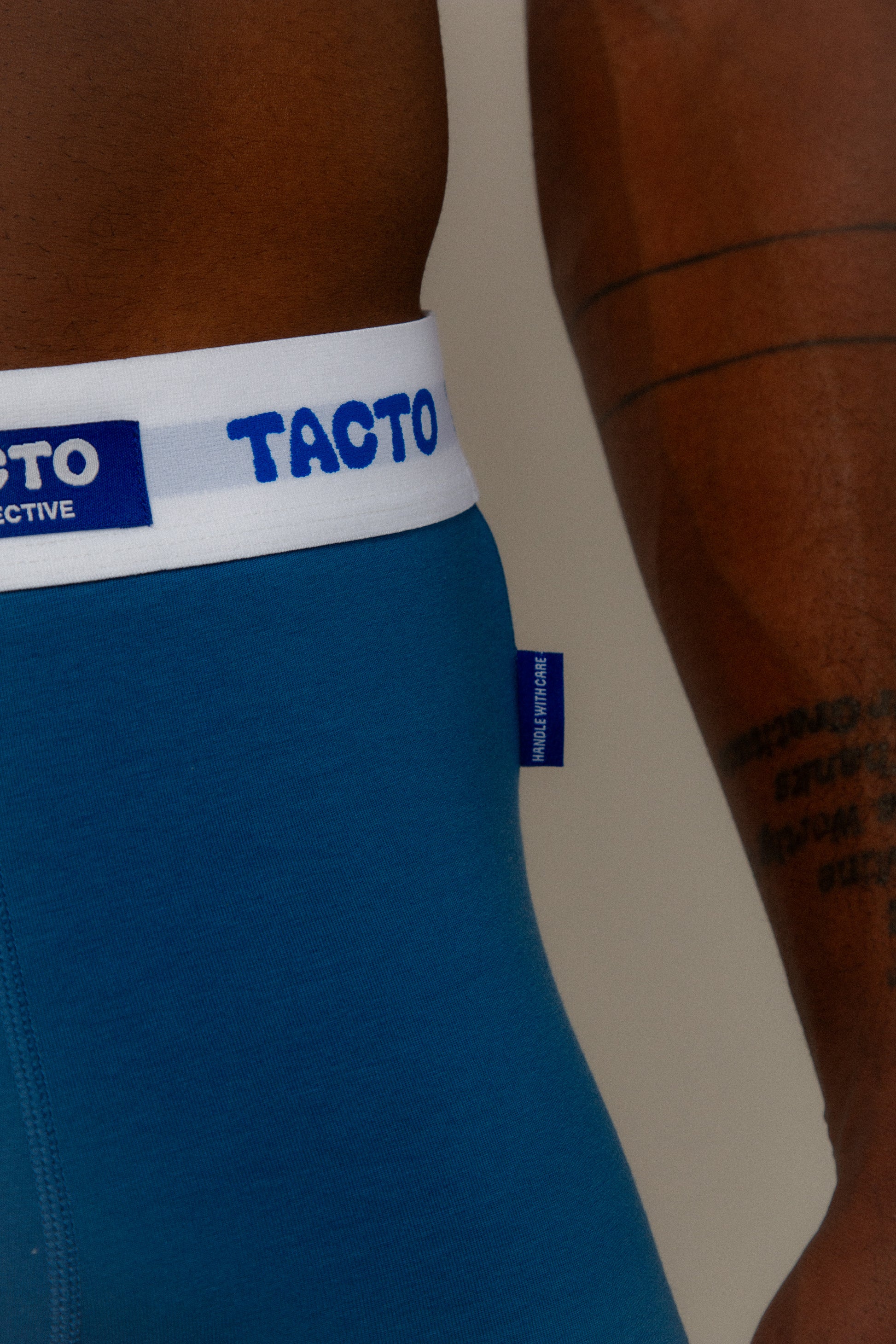 Blue athletic shorts with a white waistband featuring the 'Tacto' brand logo. TACTO Collective underwear.