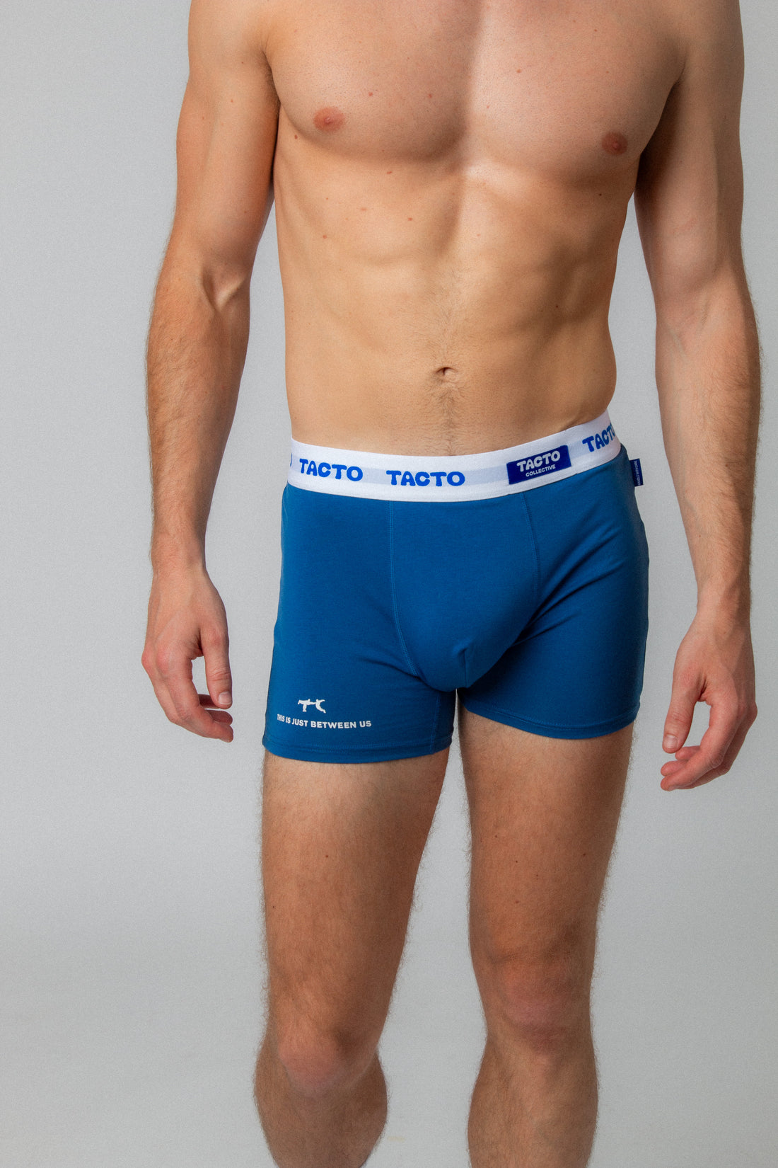 Man wearing blue boxer briefs with Tacto branding on a gray background. TACTO Collective underwear.
