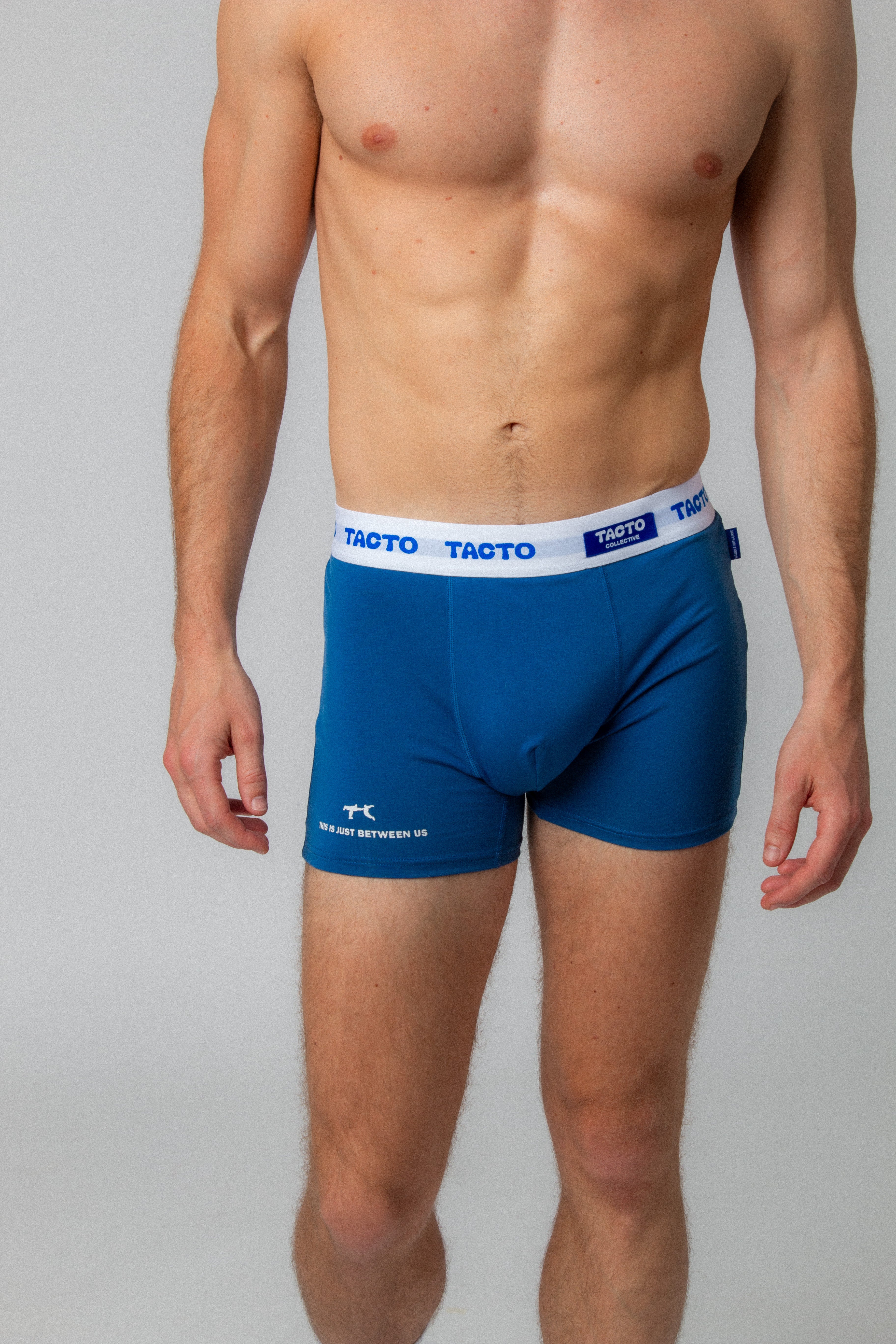 Man wearing blue boxer briefs with Tacto branding on a gray background. TACTO Collective underwear.