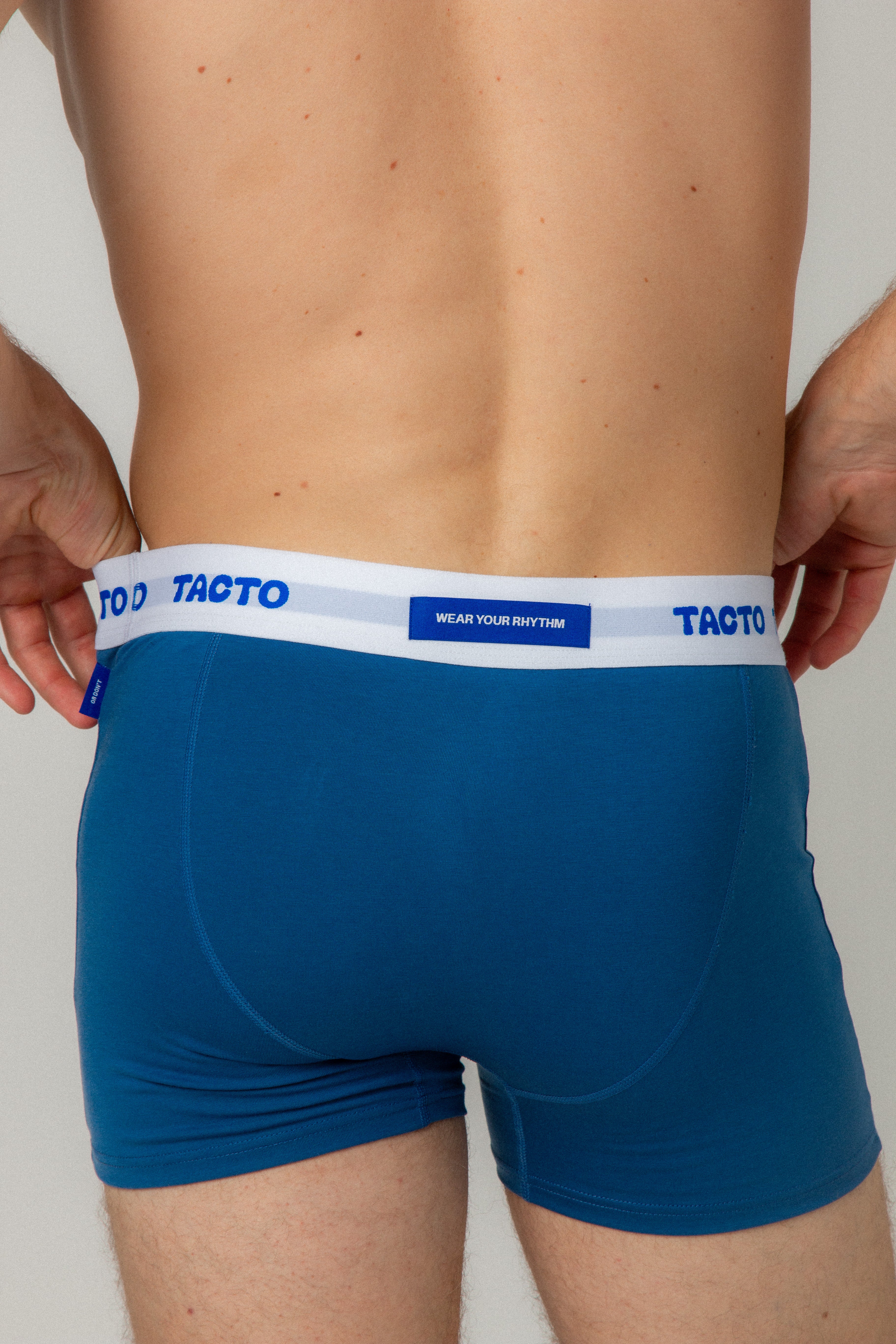 Blue boxer briefs with white waistband featuring 'Tacto' branding on a plain background. TACTO Collective underwear.