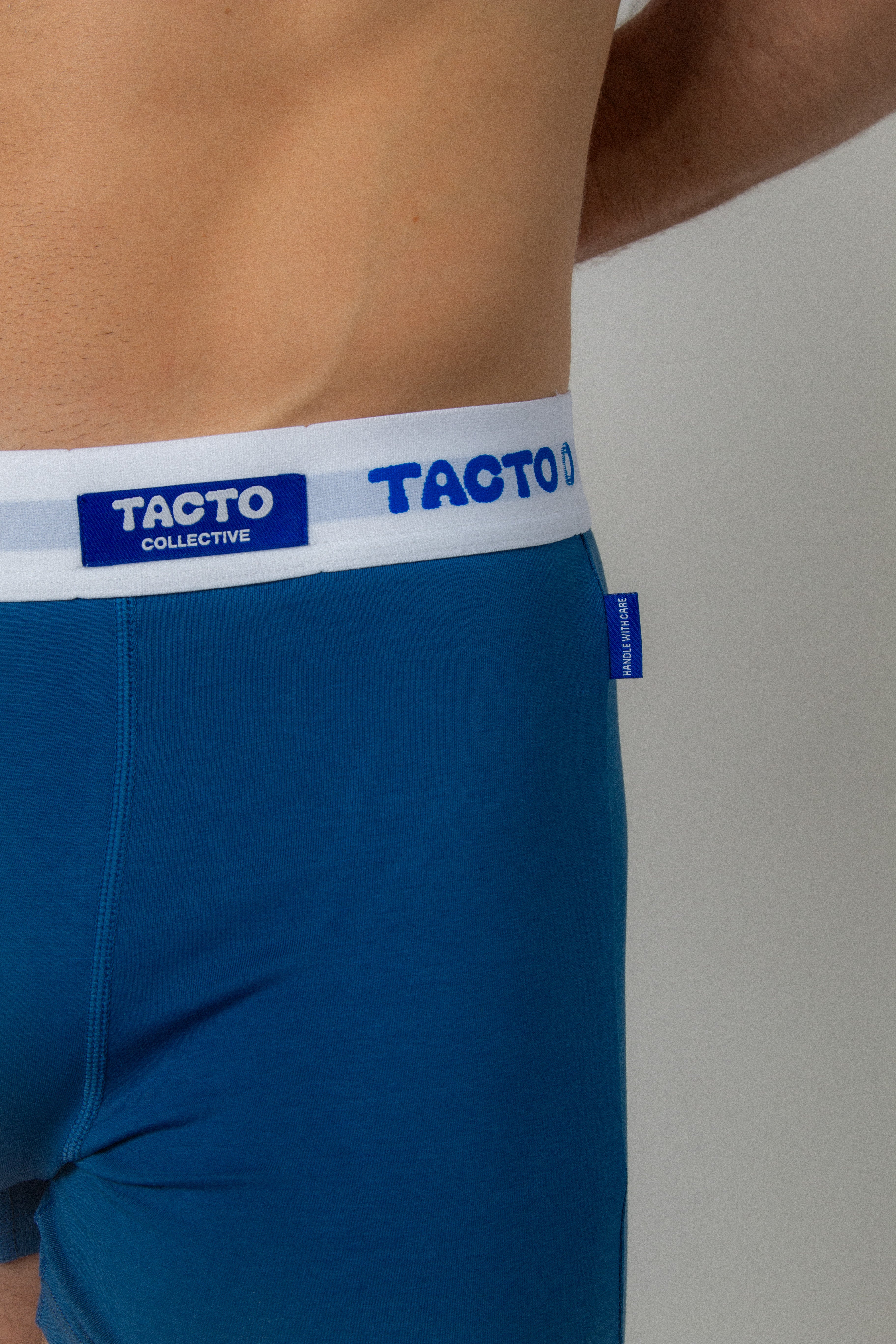 Blue boxer briefs with white waistband featuring 'TAGTO' branding on a neutral background. TACTO Collective underwear.