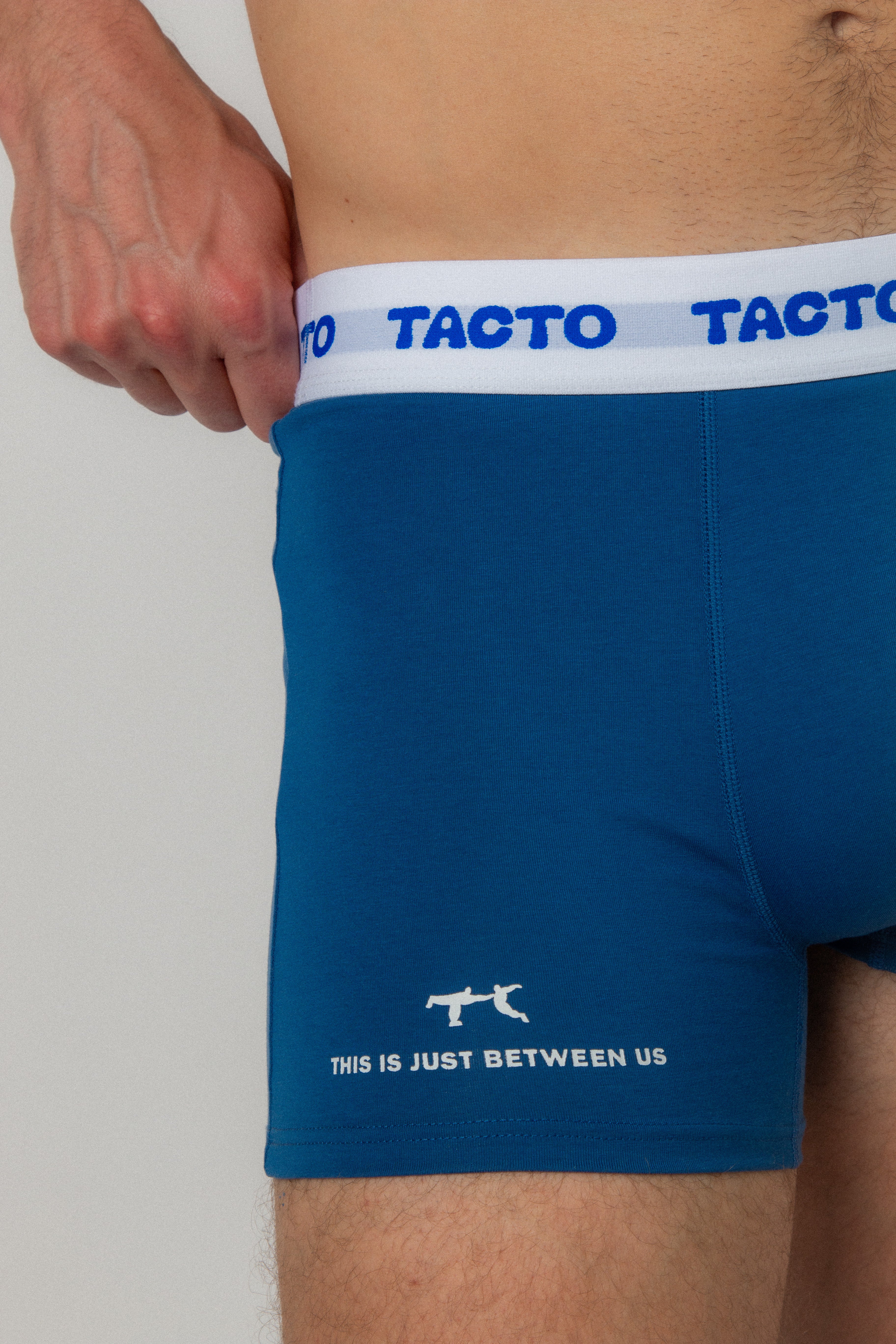 Blue boxer briefs with white waistband and text, on a plain background. TACTO Collective underwear.