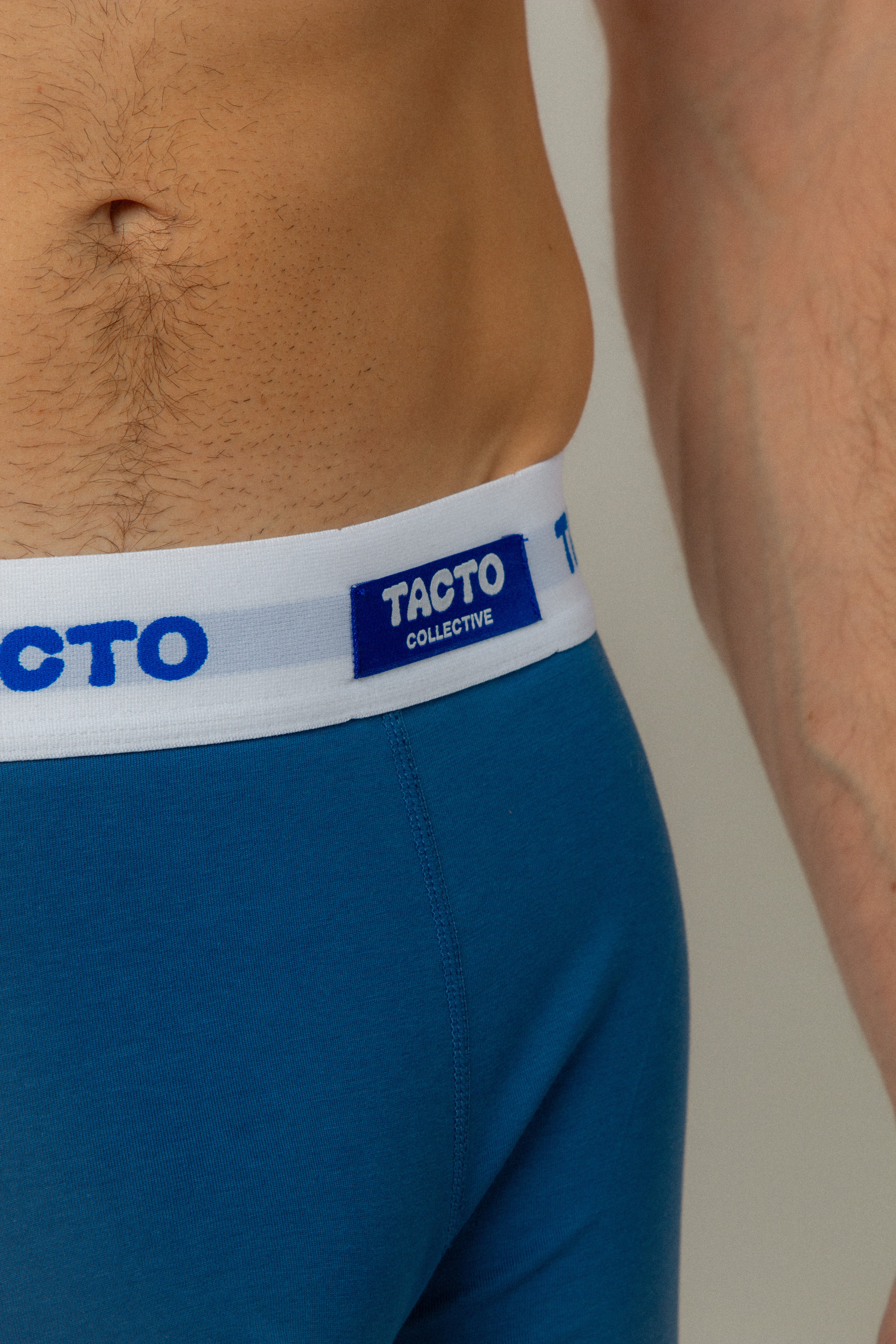 Blue underwear with a white waistband featuring 'TACTO' branding on a neutral background. TACTO Collective underwear.