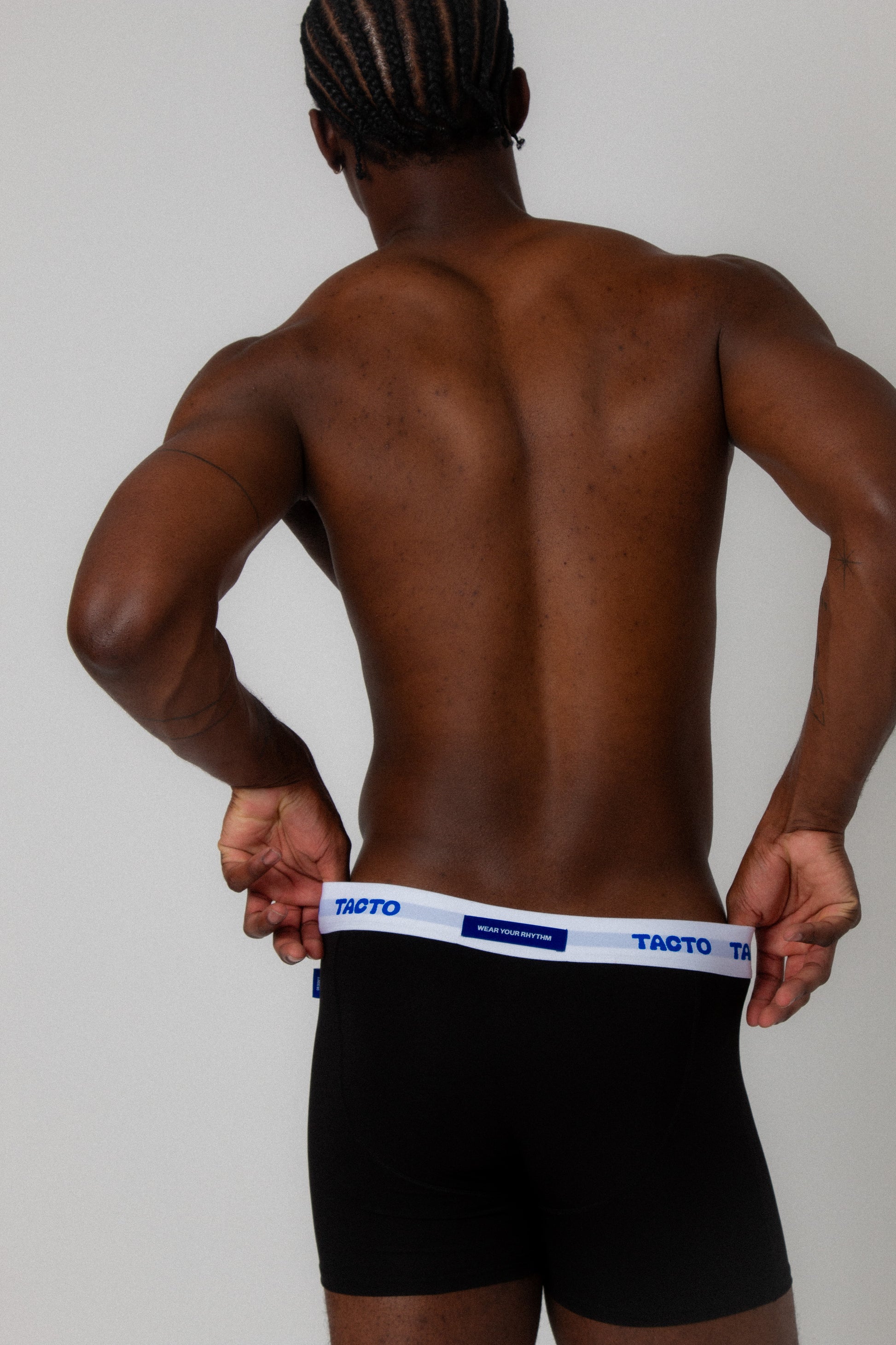 Person wearing black boxer briefs with a visible brand logo on a plain background. TACTO boxer briefs, underwear, with back tag that reads WEAR YOUR RHYTHM
