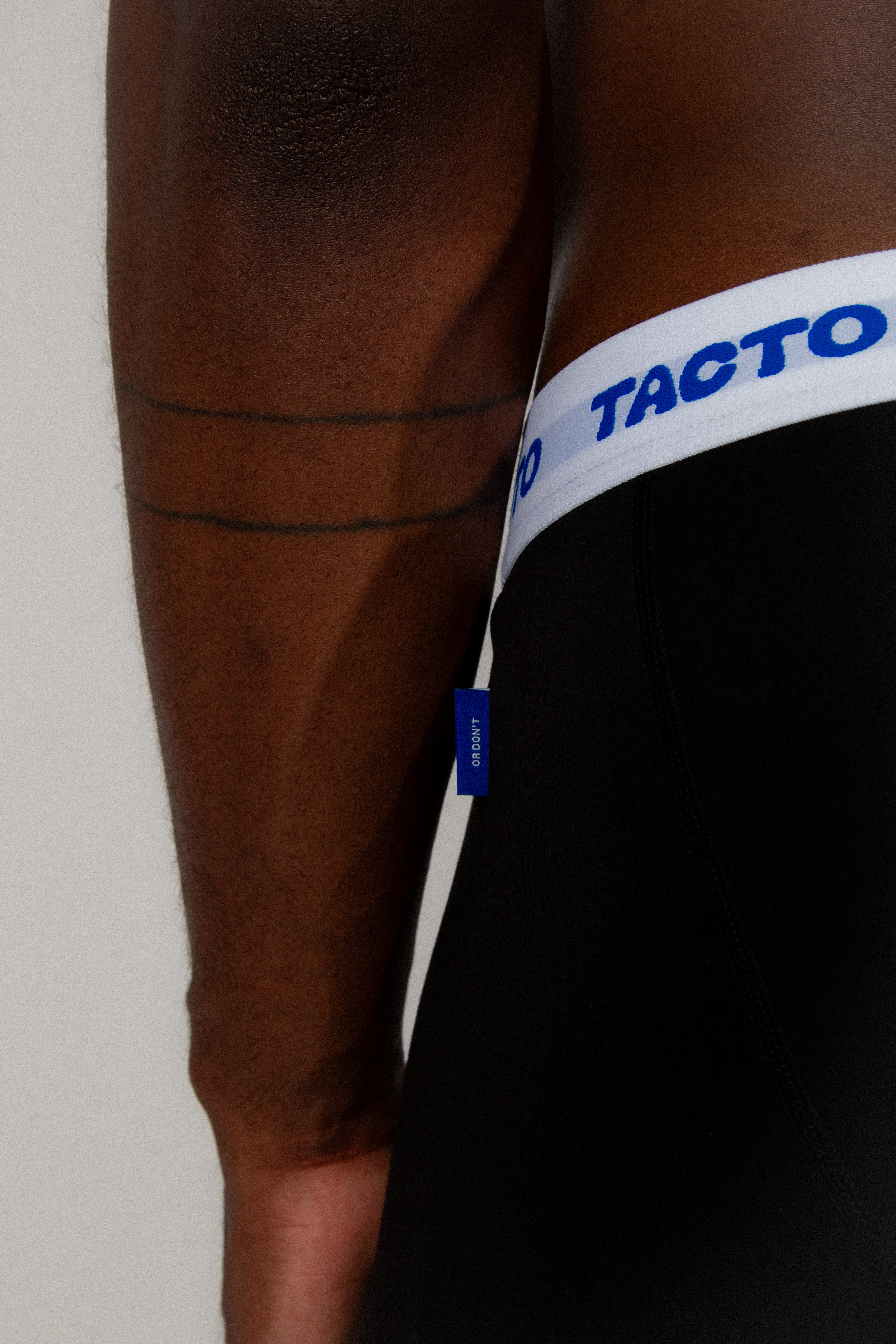 Close-up of a person wearing black shorts with a white waistband featuring 'Tacto' branding.