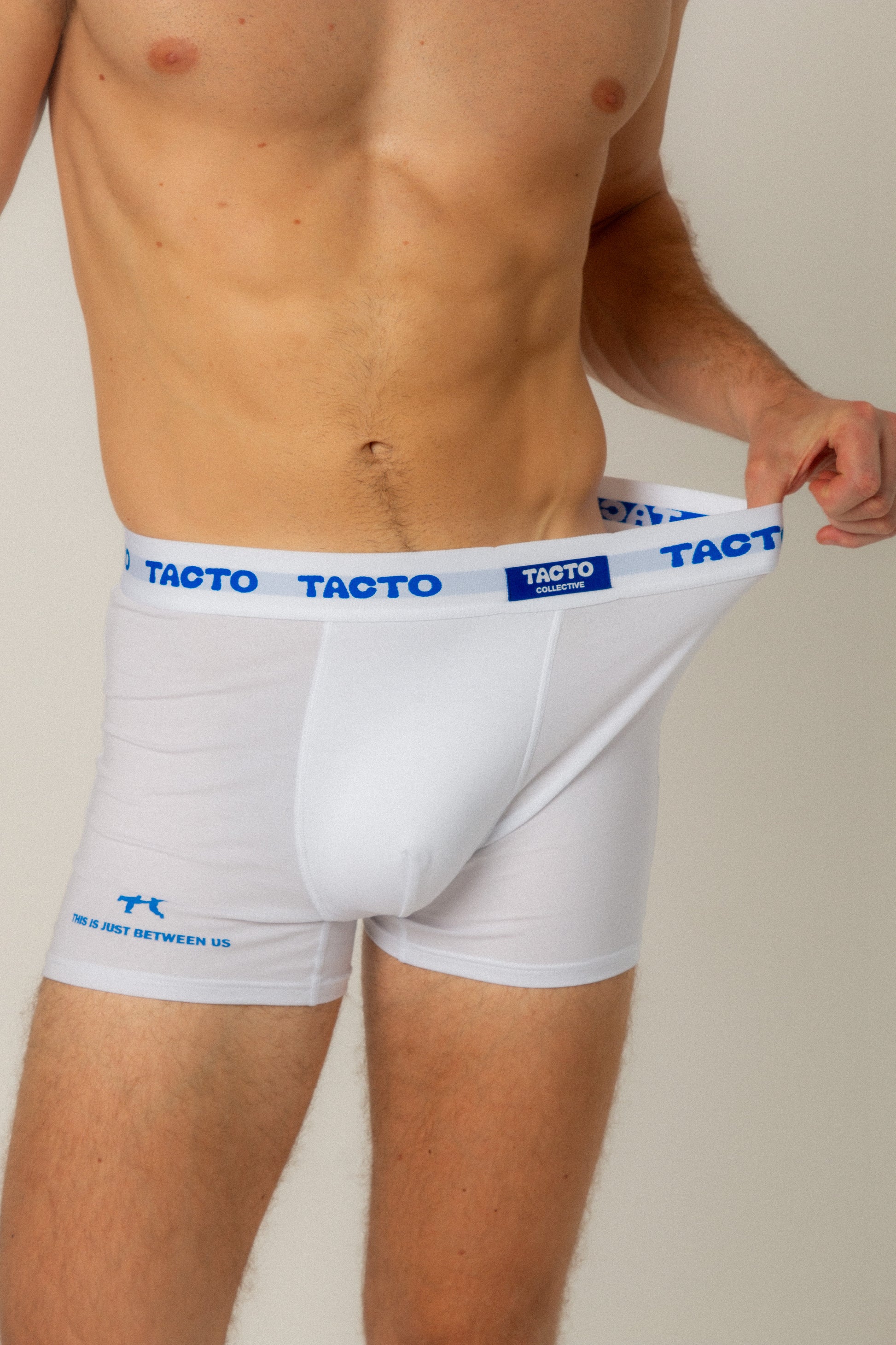 White boxer briefs with blue branding on a plain background. Tacto Collective. Stretching  waistband